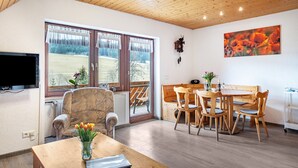 A room with a wooden ceiling, a TV mounted on the wall, a dining table with chairs, and a window with curtains. - Holiday Apartment 'Schöne Aussicht, 60sqm' with Shared Garden, Balcony and Wi-Fi (Titisee-Neustadt)
