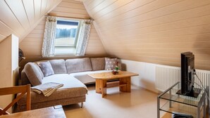 Une pièce mansardée chaleureuse avec un plafond en bois, un canapé, une table et un téléviseur posé sur un meuble en verre.