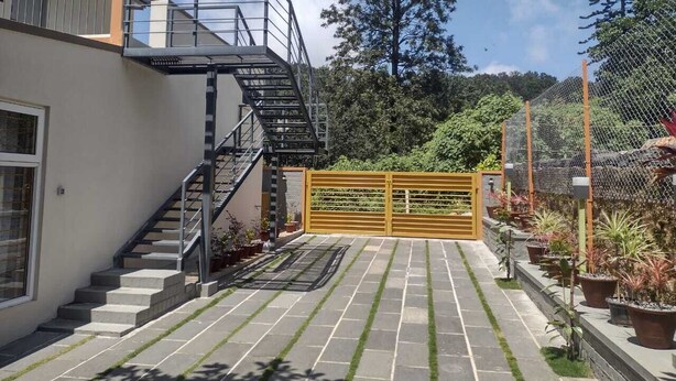 Ein Wohnhaus mit einer Treppe zu einem Balkon, einem verschlossenen Eingang und einem Gartenbereich mit Kübelpflanzen.