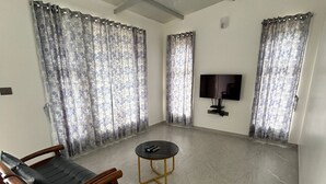 Ein geräumiges Wohnzimmer mit Deckenventilator, einer Couch, einem Couchtisch und Vorhängen.