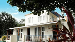 Ein zweistöckiges Haus mit einer überdachten Terrasse, einer sichtbaren Treppe und einem Swimmingpool im Hintergrund.