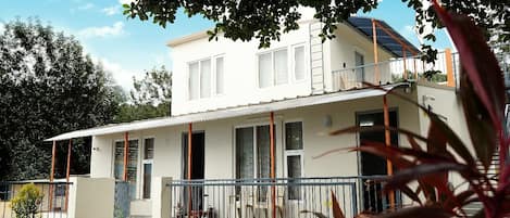 A two-story house with a covered patio, a visible staircase, and a swimming pool in the background.