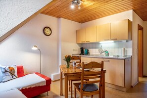 A cozy kitchen with wooden cabinets, a dining table, and a red sofa. - Apartment 'Vogelnest, 35sqm' with Shared Garden and Wi-Fi (Titisee-Neustadt)