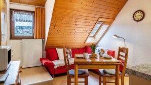 Une pièce chaleureuse avec un plafond en bois, un canapé rouge, une table à manger avec des chaises, une horloge au mur et une fenêtre avec des rideaux.