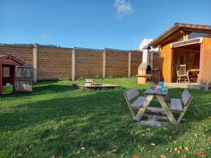 Une cabane en bois avec une cheminée, une table de pique-nique et une maisonnette pour enfants dans une cour arrière verdoyante.
