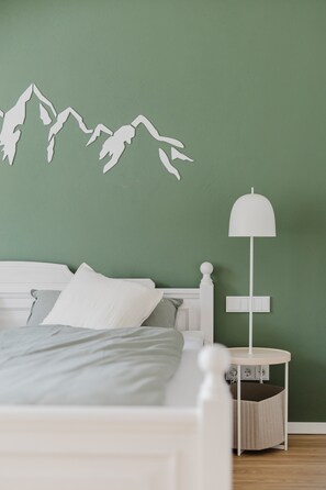 Un dormitorio con una cama, una mesita de noche con lámpara y una decoración de montañas en la pared.