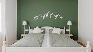 A bed with white headboard and footboard, two bedside tables, and a wall-mounted mountain design. - Apartment 'Waldzauber' with Balcony and Wi-Fi (Lennestadt)