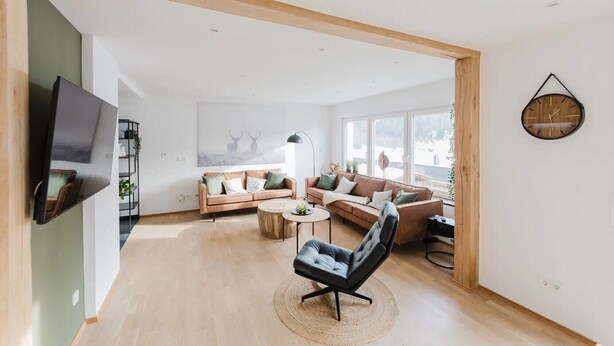 A spacious living room with a sofa set, a black leather chair, a round coffee table, and a wall-mounted clock. - Apartment 'Waldzauber' with Balcony and Wi-Fi (Lennestadt)