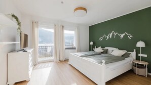 A bedroom with a bed, a bedside table, a lamp, a window with curtains, and a view of the outside. - Apartment 'Waldzauber' with Balcony and Wi-Fi (Lennestadt)
