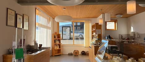 A modern interior with wooden accents, a reception desk, a display case with cheese, and a view through the window.
