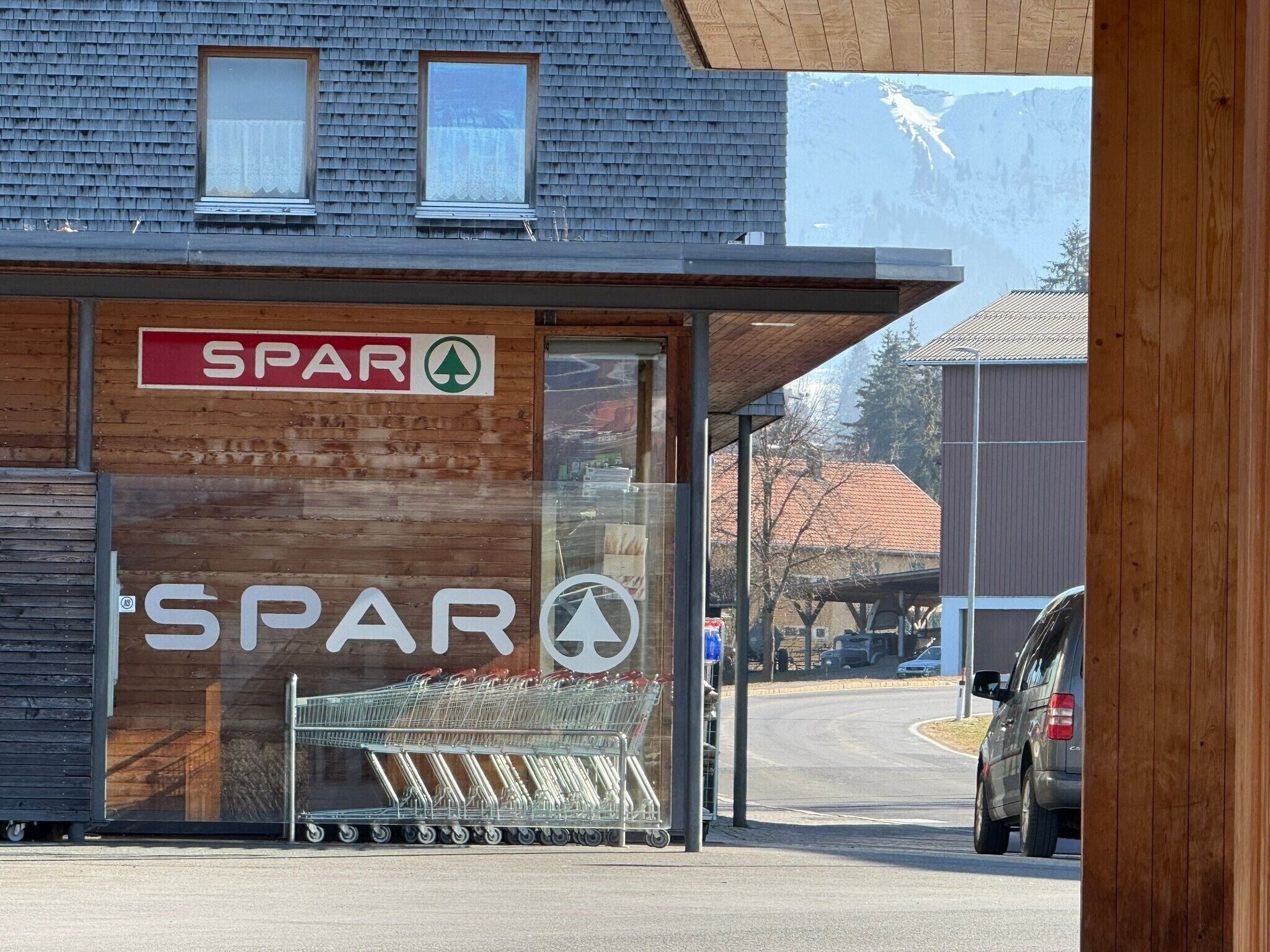 A SPAR store with a large glass window, shopping carts outside, and a view of the surrounding area.
