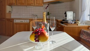 Una cocina con armarios de madera, encimera blanca y una mesa con fruta y vasos.
