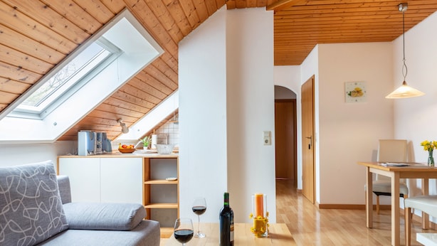 Ein modernes Interieur mit einer offenen Deckenkonstruktion, einer Couch, einem Esstisch und einer Küchenzeile.