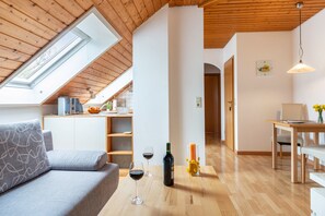 A modern interior with a loft-style ceiling, a sofa, a dining table, and a kitchen area. - Haus Annette – Apartment 'No. 2' with Balcony and Wi-Fi (Immenstaad am Bodensee)