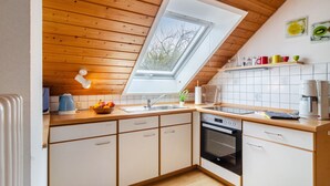 Eine Küche mit Holzbalkendecke, Oberlicht, weißen Schränken, einer Kaffeemaschine und einer Obstschale.