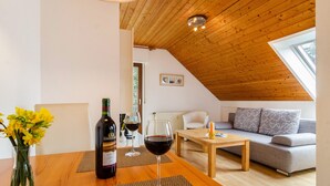 Ein gemütlicher Loftraum mit Holzbalkendecke, einer Couch, einem Couchtisch und einem Esstisch mit Weingläsern und einer Weinflasche.
