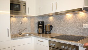 Una cocina con gabinetes blancos, un microondas de acero inoxidable, una cafetera y una estufa.