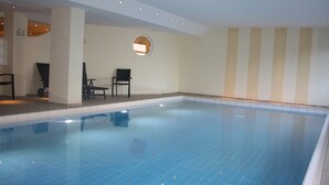 Una piscina interior con paredes de azulejos, un espejo circular y algunas sillas.
