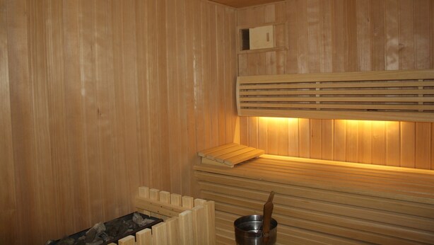 Una sauna con paredes y bancos de madera, un balde de metal y un estante de madera.