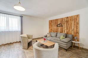 A modern living room with a grey sofa, two armchairs, a wooden coffee table, and a wooden accent wall with a mountain design.