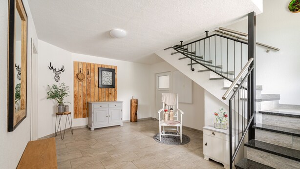 A spacious living area with a staircase, a white cabinet, a wooden wall panel, and a clock. - Bergliebe Apartment with Private Terrace and Wi-Fi (Sasbach)