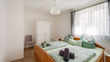 Une chambre à coucher avec un lit en bois, une armoire blanche, une chaise et une fenêtre avec des rideaux.