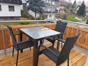 Eine Holzterrasse mit einem Glastisch und vier Korbstühlen.