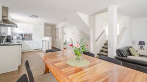 Una cocina moderna con armarios blancos, una mesa de comedor con sillas y una escalera que sube a otro nivel.