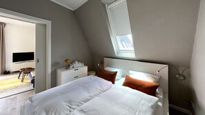 Un dormitorio con cama, mesita de noche, lámpara, televisor y ventana.