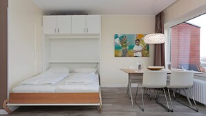 Une chambre à coucher avec un lit, un bureau, des chaises, un tableau et une fenêtre donnant sur un beau paysage.
