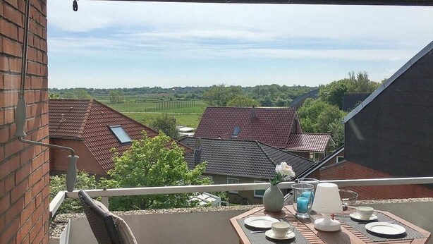 Un balcon avec une table dressée pour deux personnes, donnant sur un quartier résidentiel avec des maisons et de la verdure.