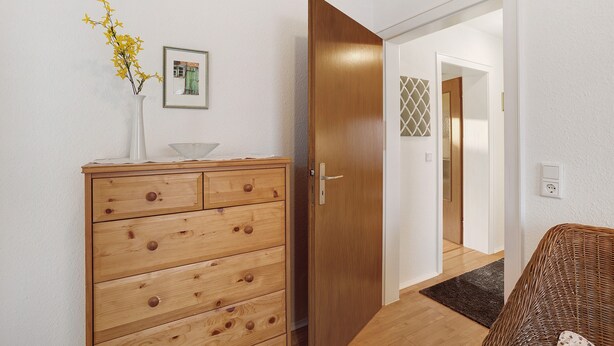 A wooden dresser with drawers, a vase with yellow flowers, a framed picture, and a wooden door leading to another room. - Holiday Apartment 'Auszeit' with Private Terrace, Shared Garden and Wi-Fi (Arnsberg)