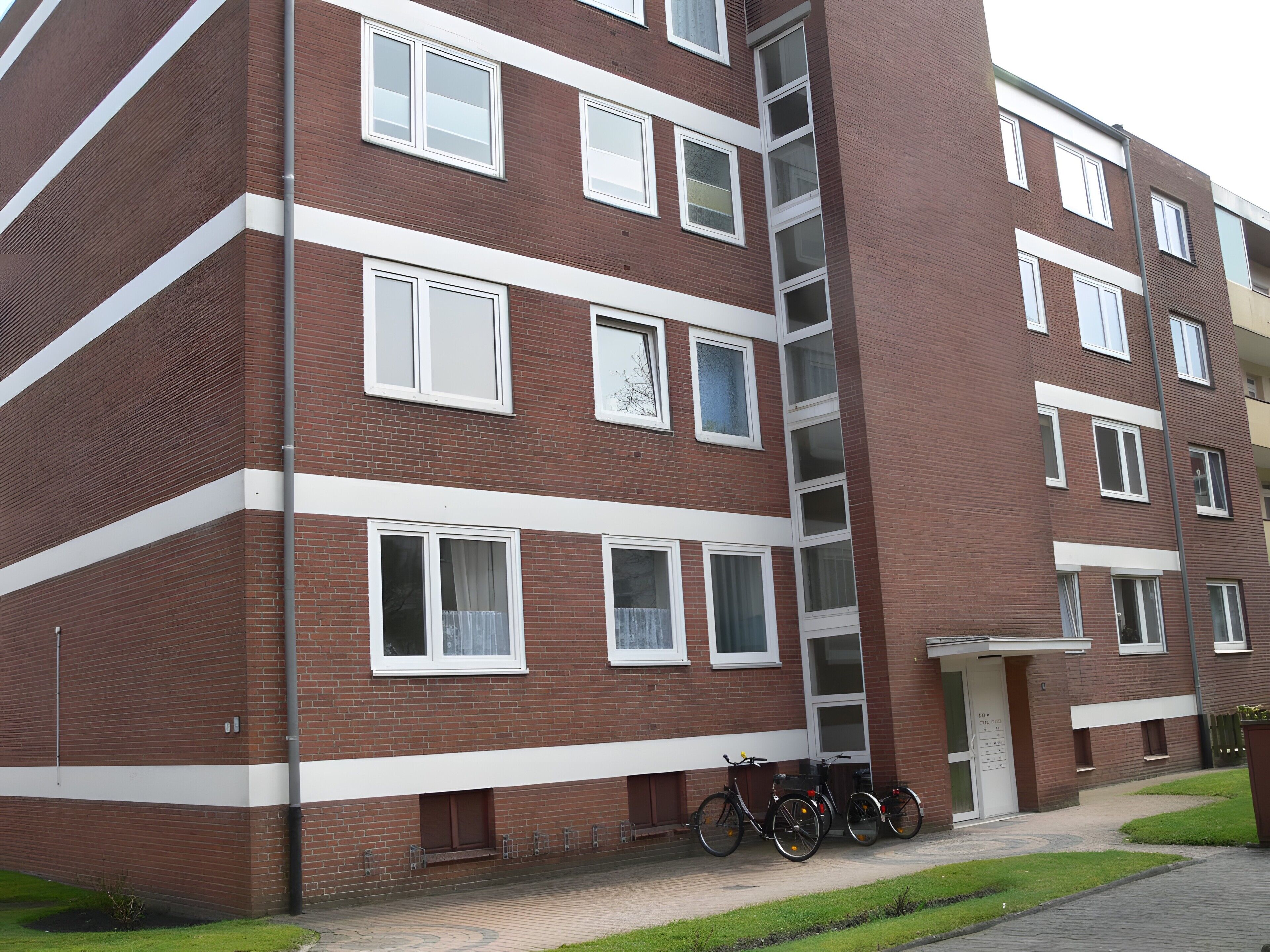 A multi-story brick building with white-framed windows, a central staircase, and bicycles parked outside.