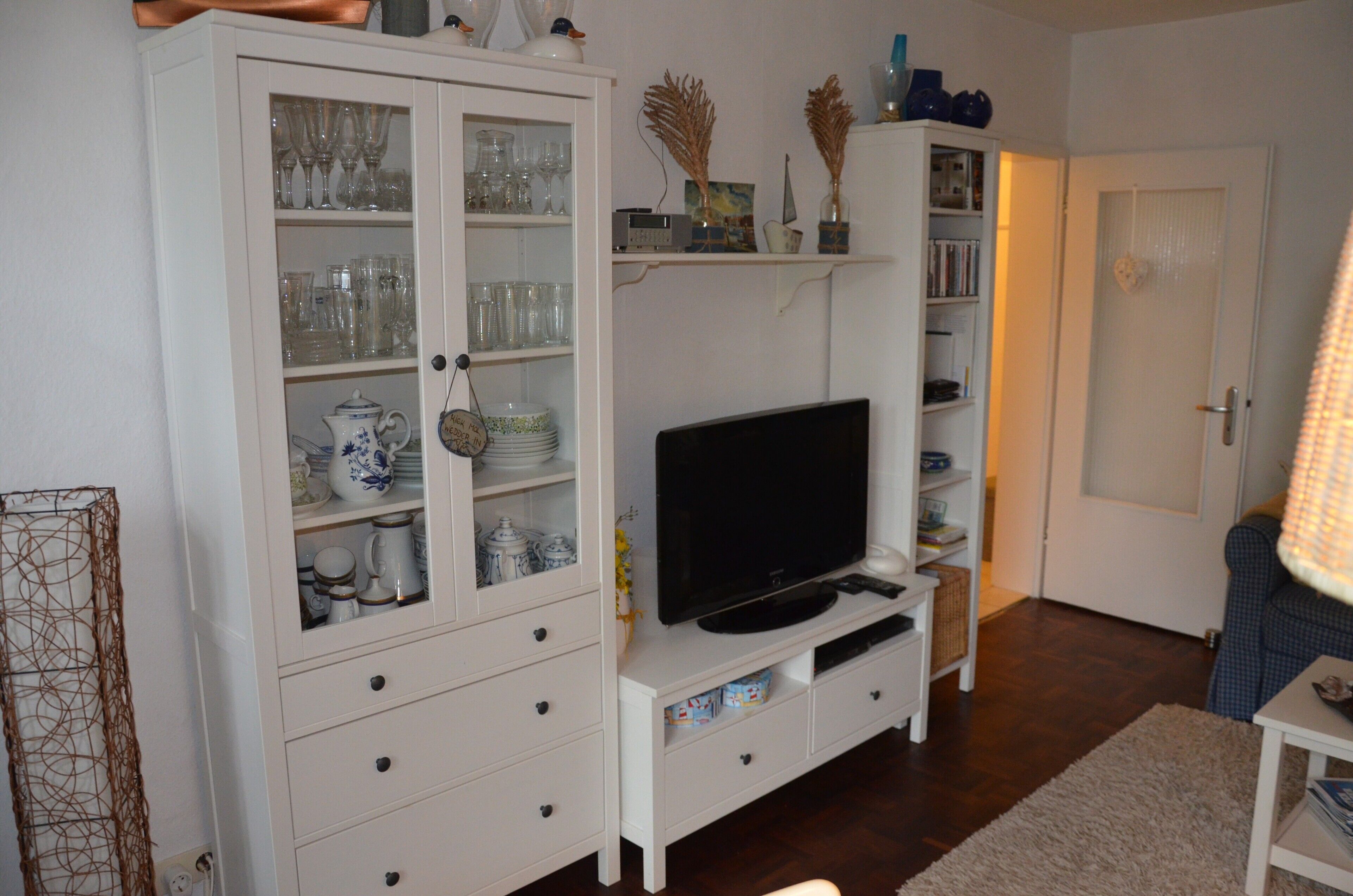 A living room with a television, white cabinets with glass doors, and a bookshelf.