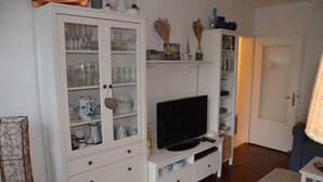 Een woonkamer met een televisie, witte kasten met glazen deuren en een boekenkast.