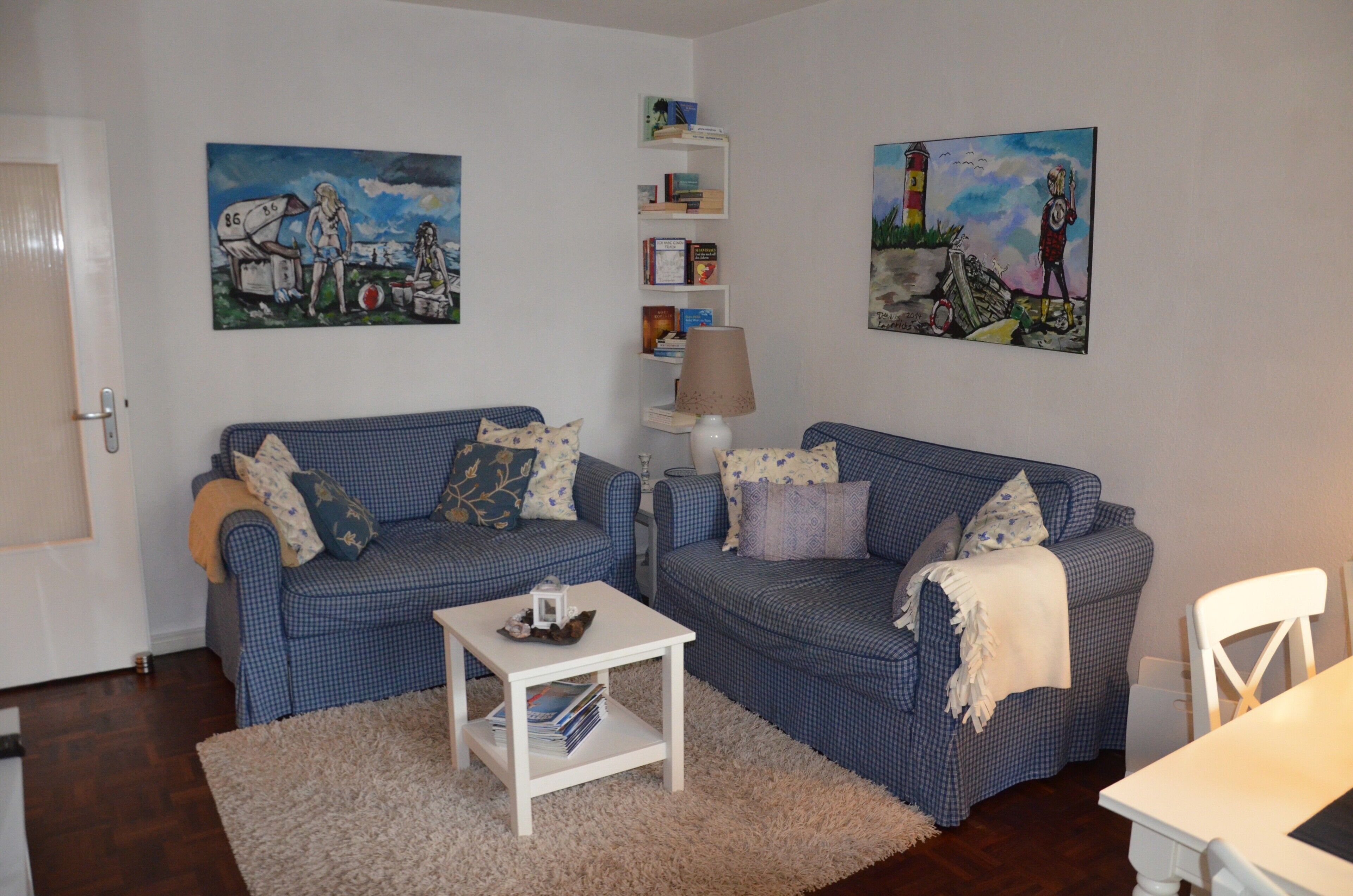 Ein Wohnzimmer mit zwei blau karierten Sofas, einem weißen Couchtisch und einem Bücherregal voller Bücher.
