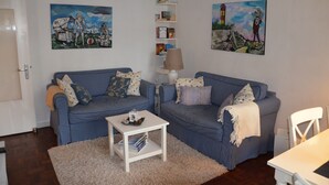 Een woonkamer met twee blauw geruite banken, een witte salontafel en een boekenkast vol boeken.