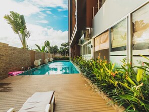 Un espace piscine extérieur moderne, doté d’une terrasse en bois, de chaises longues et de plantes tropicales.