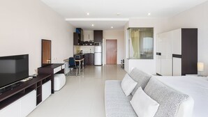 Ett modernt hotellrum med en stor säng, en TV, en soffa, ett skrivbord och ett litet kök.