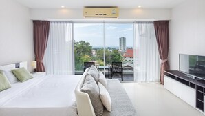 Ett modernt hotellrum med en stor säng, en soffa, en TV och utsikt över staden genom stora fönster.