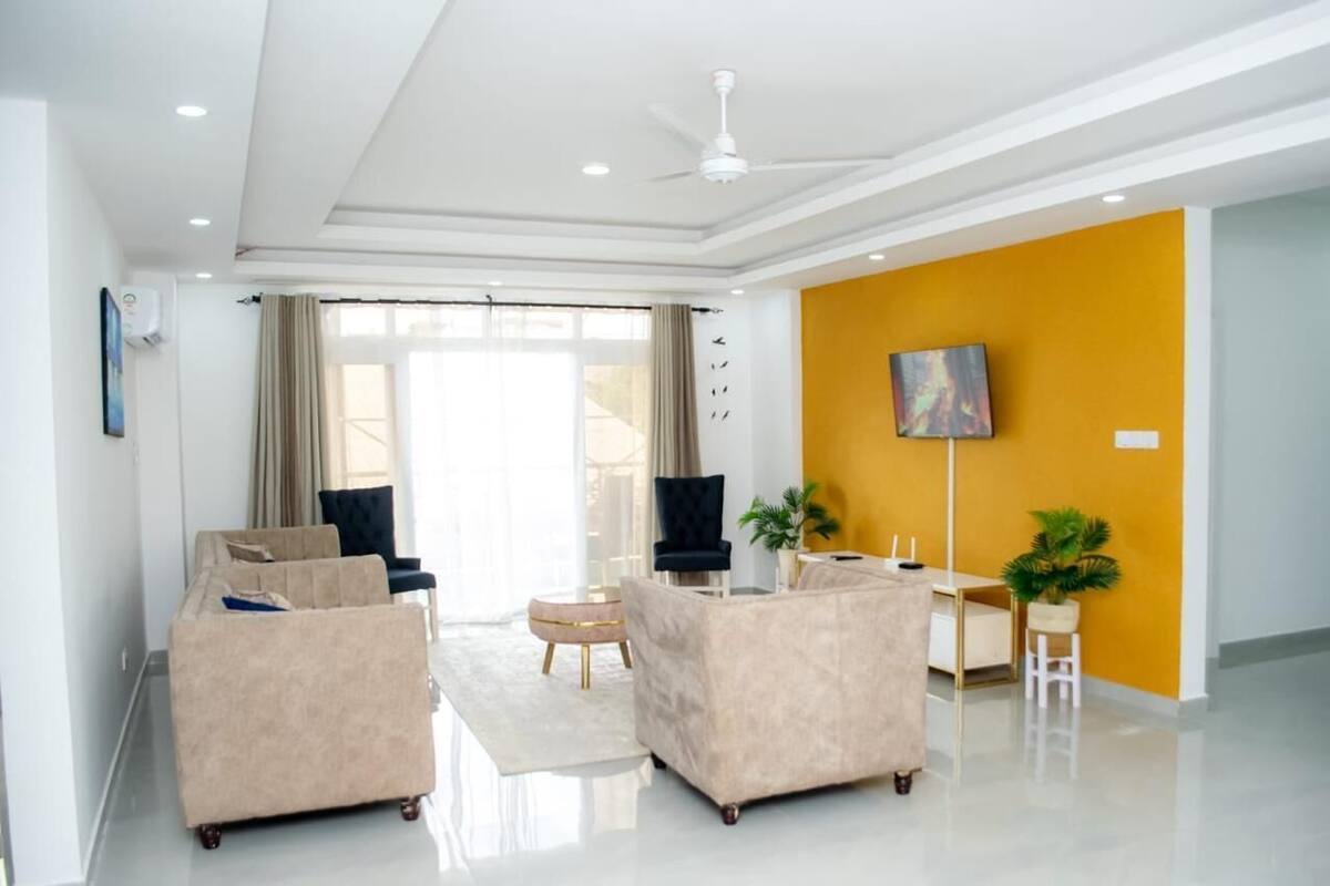 Un salón moderno con un sofá beige, una mesita de centro y un televisor montado en una pared amarilla.