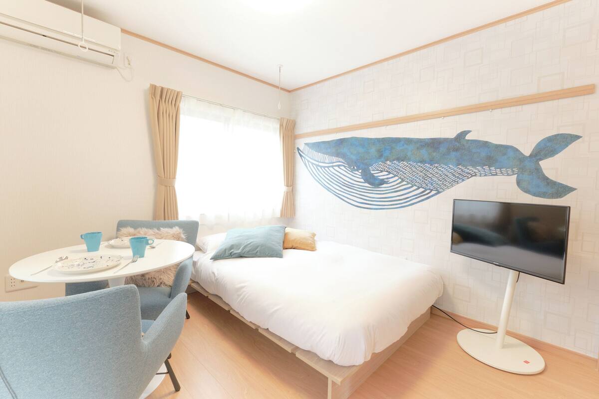 A room with a bed, a TV, a table with chairs, and a window with curtains.