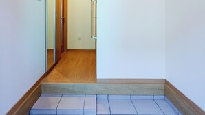 A narrow hallway with a wooden floor, white walls, and a door at the end.