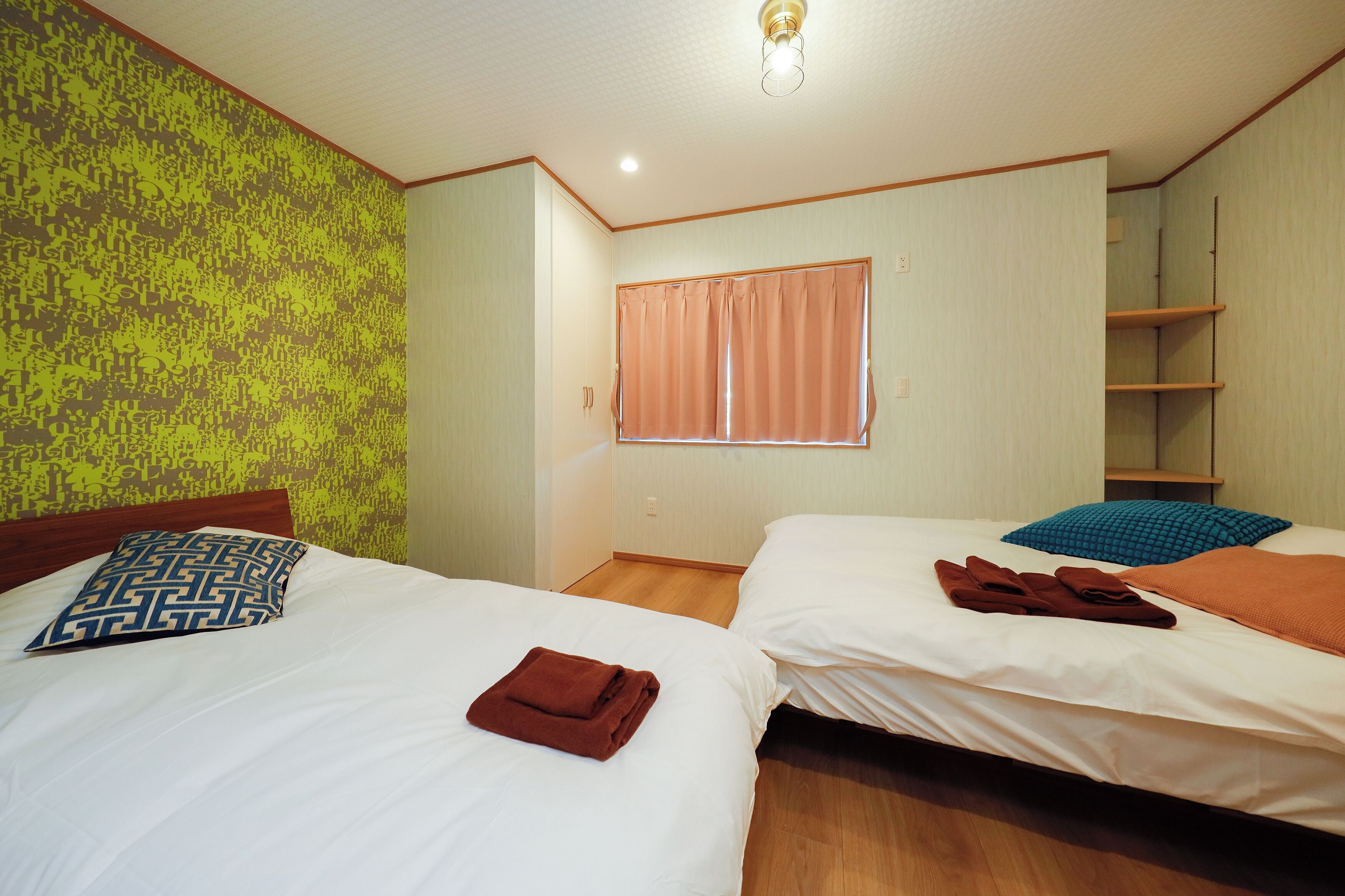 A hotel room with two beds, a window with curtains, a wooden floor, and a green patterned wall.