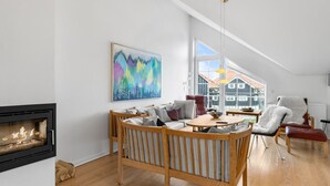 Un salon spacieux avec une cheminée, un coin repas et une vue sur les maisons grâce  à de grandes fenêtres.
