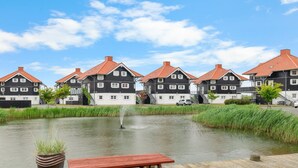 Une rangée de maisons traditionnelles aux toits rouges, une jetée en bois avec un banc, et un petit étang avec une fontaine.