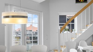 Un espace repas moderne avec une grande table, des chaises blanches et un escalier avec des marches en bois.
