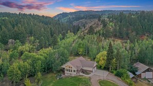 A single-story house with a large front porch, surrounded by a forested area and a hilly landscape. - Grand View Ranch | 500+ Acres, Hot Tub, Sleeps 25, Forest Access! (Tetonia)