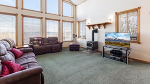 A spacious living room with a large window, a fireplace, a sofa, and a television. - Grand View Ranch | 500+ Acres, Hot Tub, Sleeps 25, Forest Access! (Tetonia)