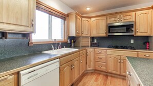 A kitchen with wooden cabinets, a built-in microwave, a dishwasher, and a window with blinds. - Grand View Ranch | 500+ Acres, Hot Tub, Sleeps 25, Forest Access! (Tetonia)